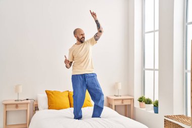 Young bald man smiling confident dancing on bed at bedroom