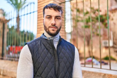 Young hispanic man with serious expression standing at street