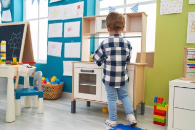 Adorable hispanic boy playing with play kitchen standing at kindergarten