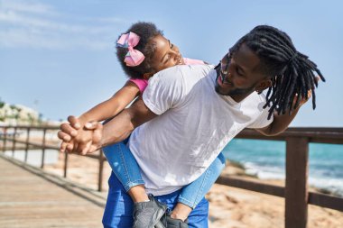 Father and daughter smiling confident holding girl on back at seaside