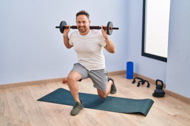 Young caucasian man smiling confident training legs exercise at sport center