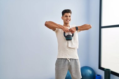 Genç İspanyol adam gülümsüyor spor merkezinde kettlebell kullanıyor.