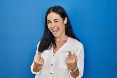 Young hispanic woman standing over blue background showing middle finger doing fuck you bad expression, provocation and rude attitude. screaming excited 