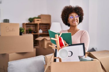 Afro-Amerikalı bir kadın gülümseyerek evde kendinden emin bir şekilde kitap okuyor.