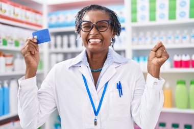 Eczanede çalışan Afrikalı kadın elinde kredi kartıyla gururla bağırıyor zaferi ve başarıyı kutluyor. 