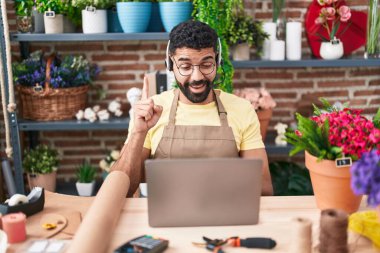 Hispanic man with beard working at florist shop doing video call smiling with an idea or question pointing finger with happy face, number one 
