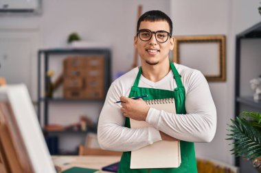 Genç sanatçı gülümsüyor. Sanat stüdyosunda kendine güvenen bir not defteri.