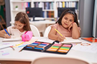 Two kids preschool students sitting on table drawing on paper at classroom