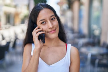 Genç, güzel, İspanyol bir kadın gülümsüyor ve caddede akıllı telefondan konuşuyor.