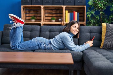 Evdeki kanepede uzanmış akıllı telefon kullanan genç, güzel İspanyol kadın.