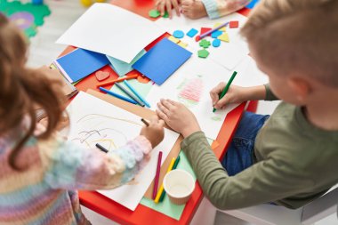 Two kids preschool students sitting on table drawing on paper at kindergarten