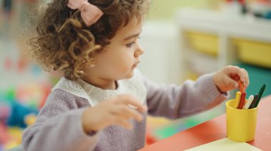 Adorable hispanic girl preschool student sitting on table drawing on paper at kindergarten