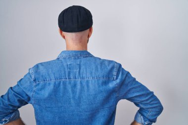 Sakallı İspanyol bir adam izole edilmiş arka planda dikilip kollarını vücuduna dayamış geriye bakıyor. 