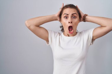 Beautiful brunette woman standing over isolated background crazy and scared with hands on head, afraid and surprised of shock with open mouth 