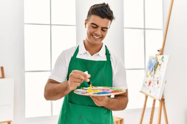 Genç İspanyol adam gülümsüyor. Sanat stüdyosunda kendine güvenen bir renk karışımı.