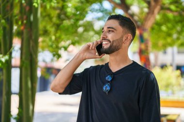 Genç Arap adam gülümsüyor. Parktaki akıllı telefondan konuşuyor.