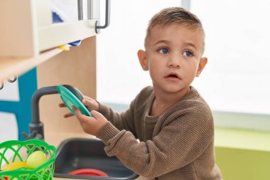 Adorable hispanic boy playing with play kitchen standing at kindergarten