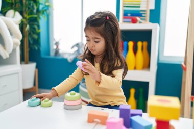 Anaokulundaki masada oturan, inşaat bloklarıyla oynayan sevimli İspanyol kız.