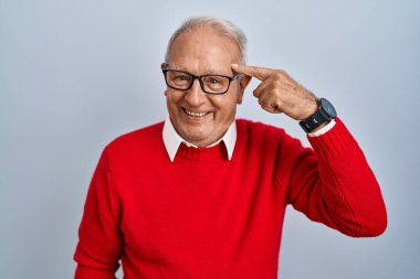 Senior man with grey hair standing over isolated background smiling pointing to head with one finger, great idea or thought, good memory 
