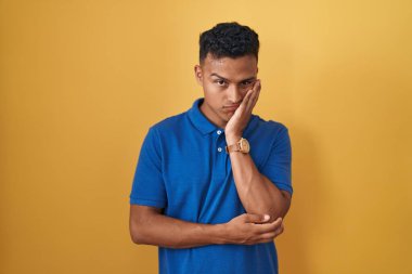 Sarı arka planda duran İspanyol genç adam çapraz kollarla depresyon sorunlarından yorgun ve sıkılmış göründüğünü düşünüyor.. 