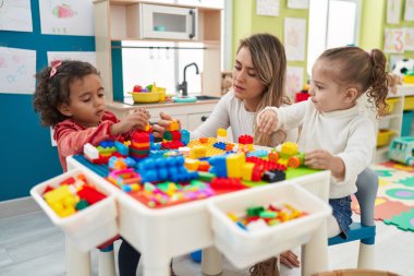 Teacher with girls playing with construction blocks sitting on table at kindergarten