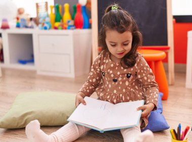 Anaokulunda yerde oturmuş kitap okuyan sevimli İspanyol kız.