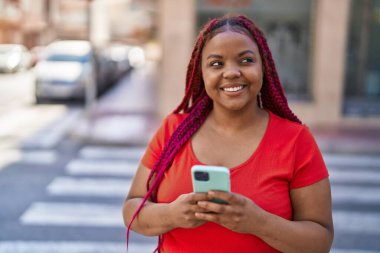 Afro-Amerikalı kadın sokakta akıllı telefon kullanarak kendine güveniyor.