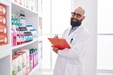 Young bald man pharmacist smiling confident writing on clipboard at pharmacy