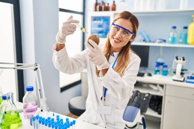 Laboratuvarda kivi enjekte eden bilim adamı üniforması giyen genç sarışın kadın.