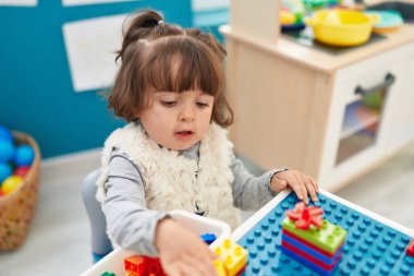 Adorable hispanic toddler playing with construction blocks sitting on table at kindergarten