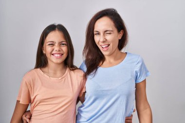 Young mother and daughter standing over white background winking looking at the camera with sexy expression, cheerful and happy face. 