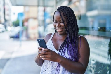 Afro-Amerikalı kadın sokakta akıllı telefon kullanarak kendine güveniyor.