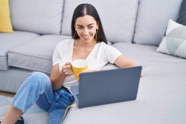 Genç İspanyol kadın evde kahve içerken dizüstü bilgisayar kullanıyor.