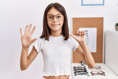 Young hispanic girl wearing glasses showing and pointing up with fingers number six while smiling confident and happy. 