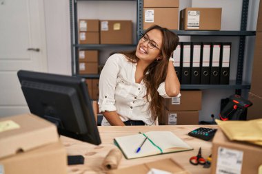 Young hispanic woman working at small business ecommerce smiling confident touching hair with hand up gesture, posing attractive and fashionable 