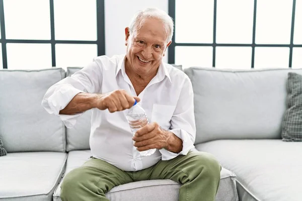 Senior man drinking bottle of water sitting on sofa at home