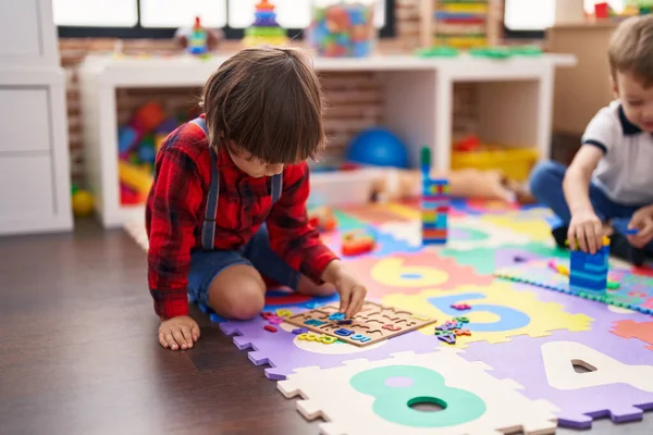建設ブロックと数学のパズルゲームで遊んでいる2人の子供が幼稚園で床に座っている — ストック写真