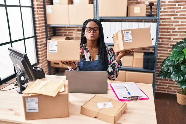 African woman with braids working at small business ecommerce holding packages looking at the camera blowing a kiss being lovely and sexy. love expression.