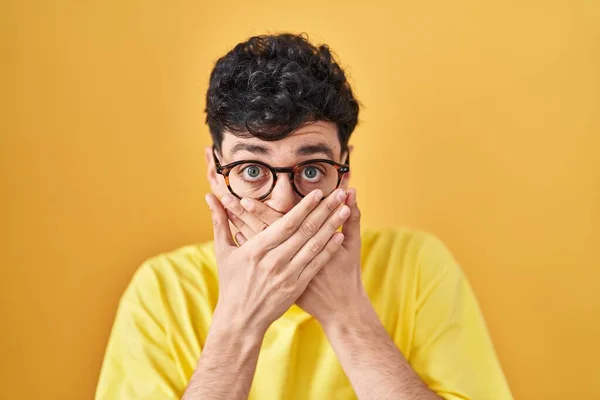 Hispanic Man Wearing Glasses Standing Yellow Background Shocked Covering Mouth — Stockfoto