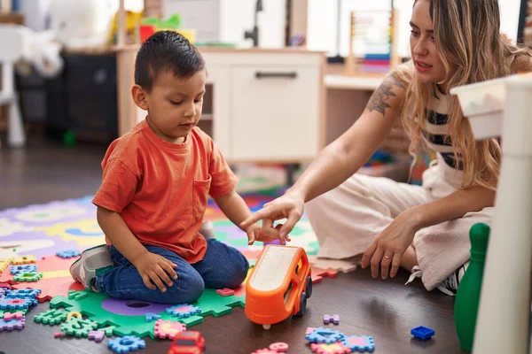 Teacher and toddler playing with cars toy sitting on floor at kindergarten