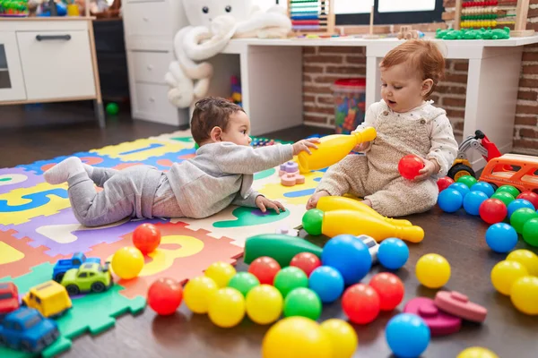 二人の可愛い赤ちゃんはボールとボウリングピンで遊んでいます床に座って幼稚園 — ストック写真