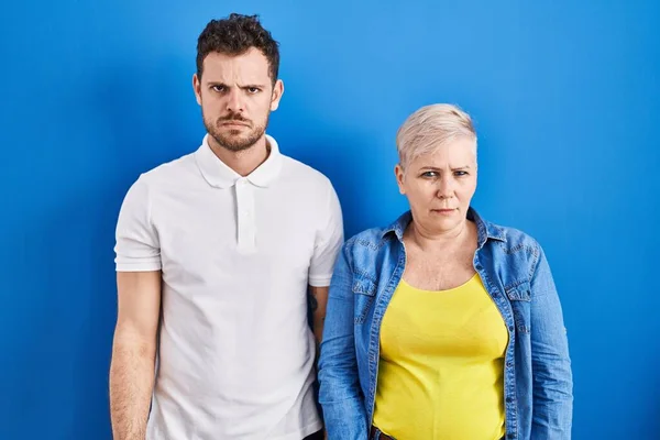 若いブラジル人の母親と息子の青の背景懐疑的で神経の上に立って 問題のために動揺を眉をひそめて 否定的な人 — ストック写真
