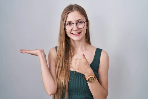 Young caucasian woman standing over white background showing palm hand and doing ok gesture with thumbs up, smiling happy and cheerful
