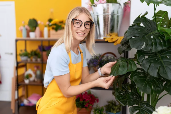 Young Blonde Woman Florist Smiling Confident Touching Sheet Plant Flower — Stock fotografie
