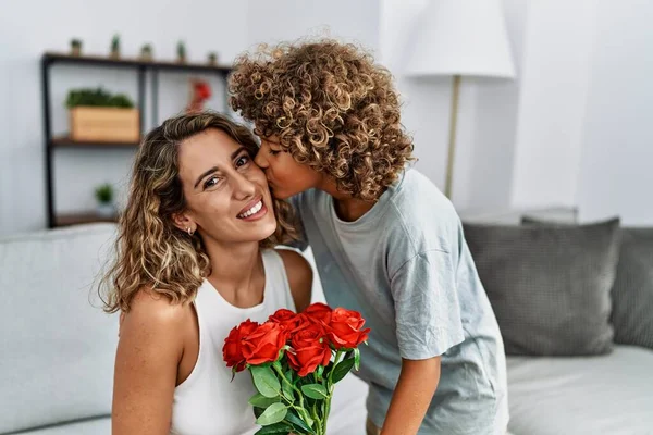 Mother and son kissing and hugging each other holding flowers at home