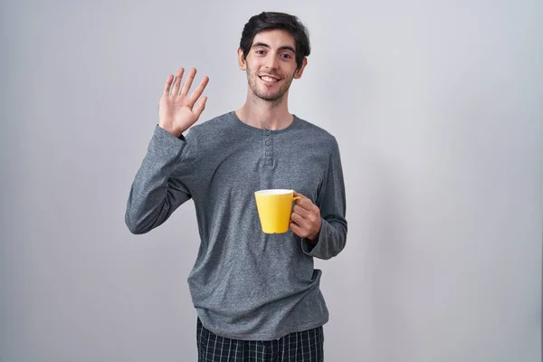 Young Hispanic Man Wearing Pajama Drinking Cup Coffee Waiving Saying — Stockfoto