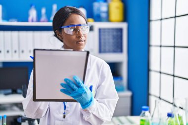 Young african american woman scientist writing on document at laboratory