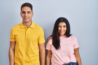 Young couple standing over isolated background winking looking at the camera with sexy expression, cheerful and happy face. 
