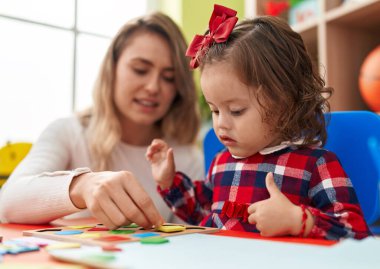 Teacher and toddler playing with maths puzzle game sitting on table at kindergarten