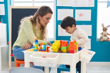 Teacher and toddler playing with construction blocks sitting on table at kindergarten